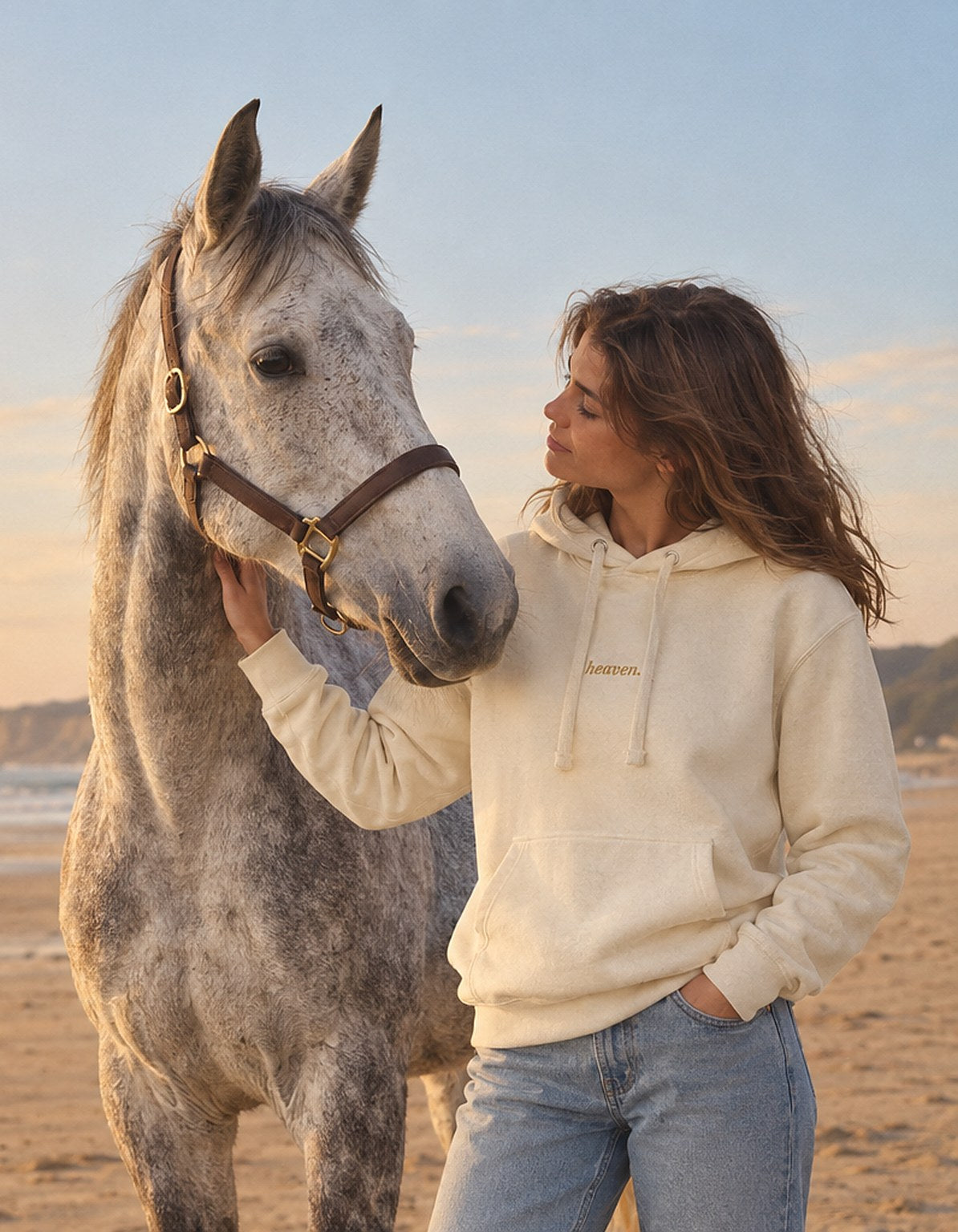 Cavalière en sweat heaven. crème à côté de son cheval gris sur une plage au coucher du soleil